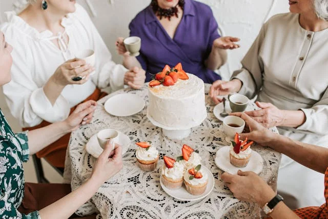 Group of friends sitting around a table eating cake and drinking coffee
